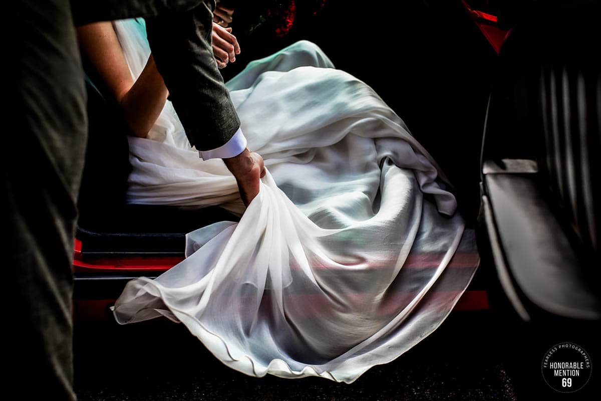 Braut steigt ins Auto ein und ihr Bräutigam hilft ihr mit dem Kleid. Honorable Mention FEARLESS. Hochzeitsfotografin Remscheid bildsprache Sina Frantzen